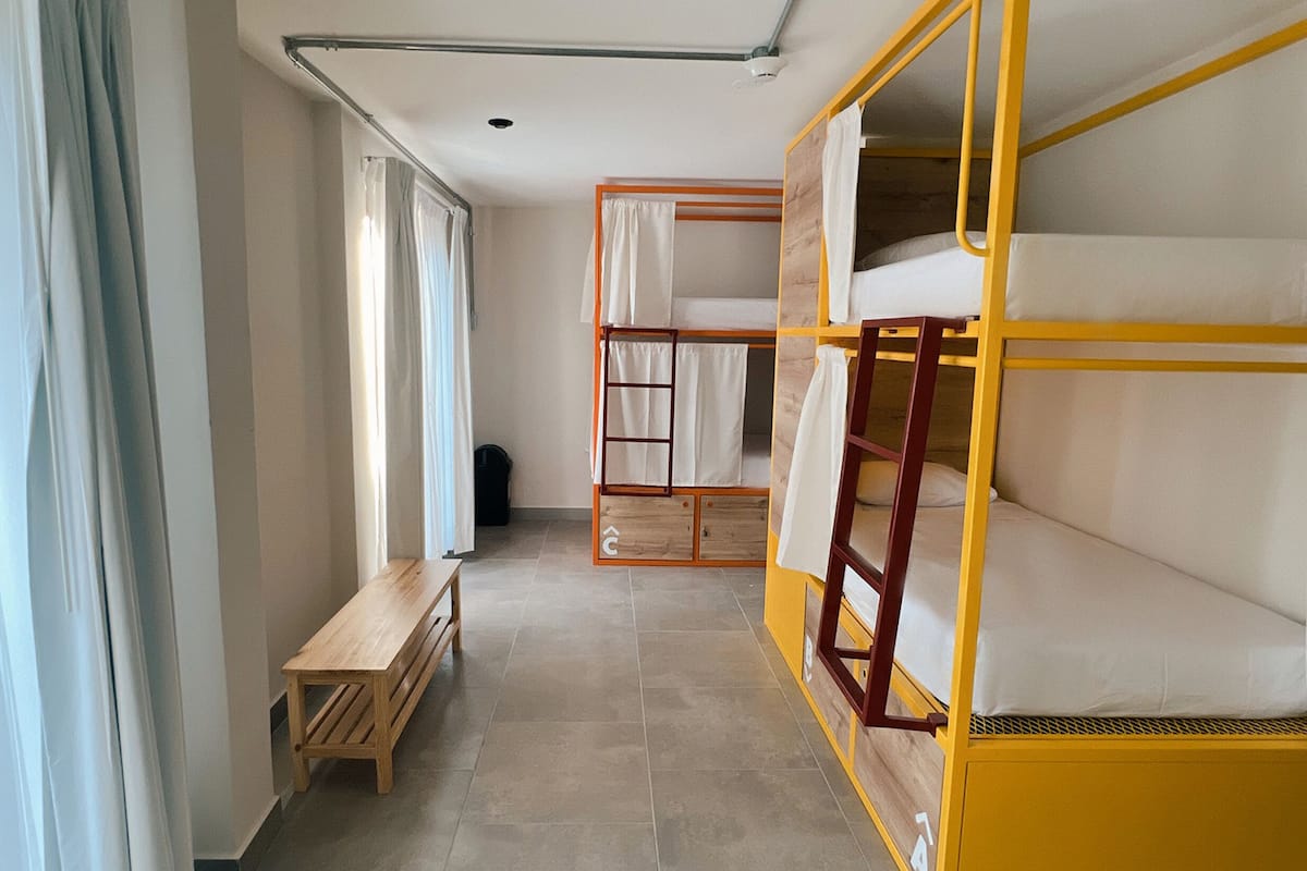A dormitory room with bunk beds, a wooden bench, and a tiled floor.