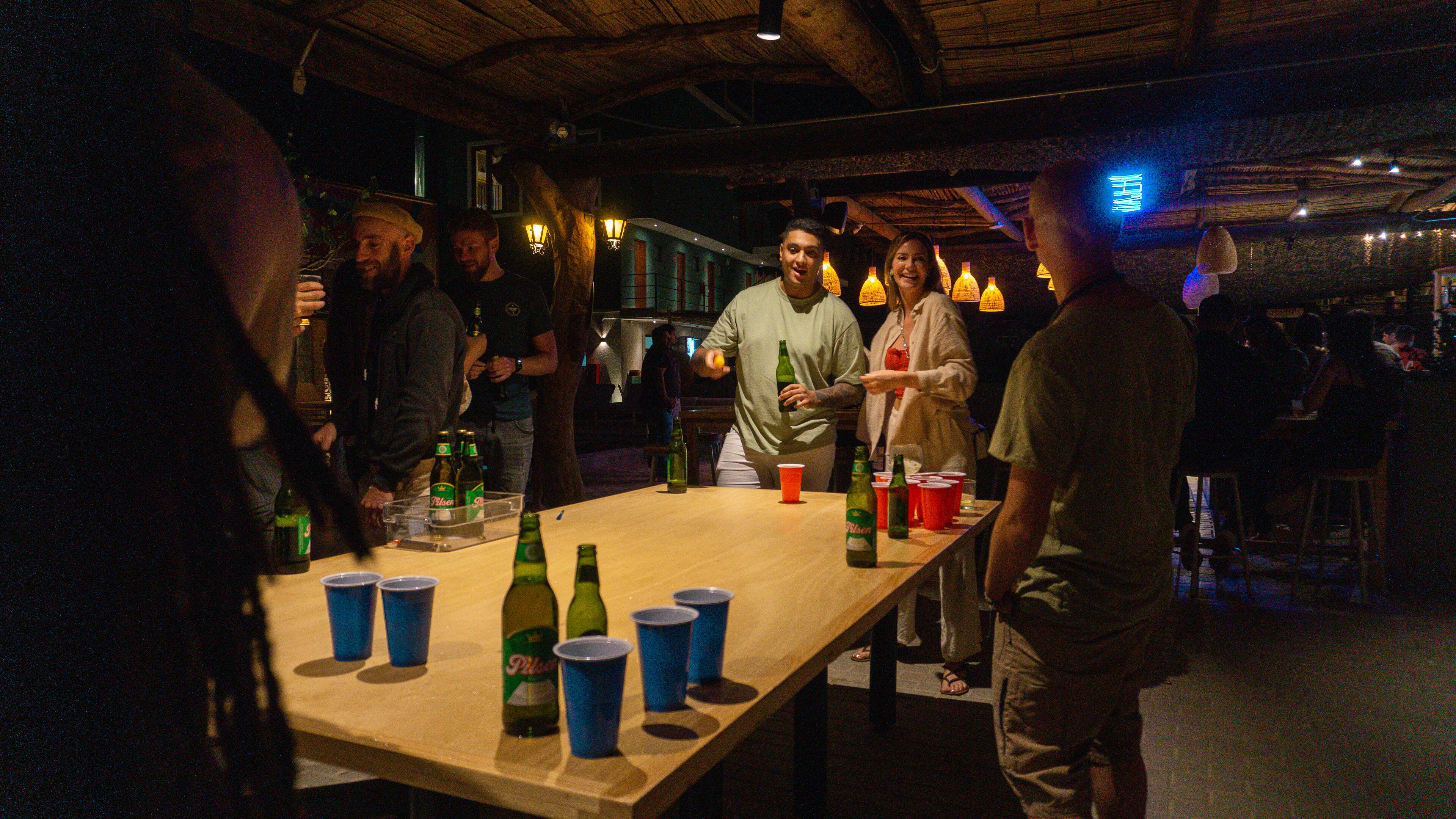 A bar area with a wooden table, bottles, and cups.