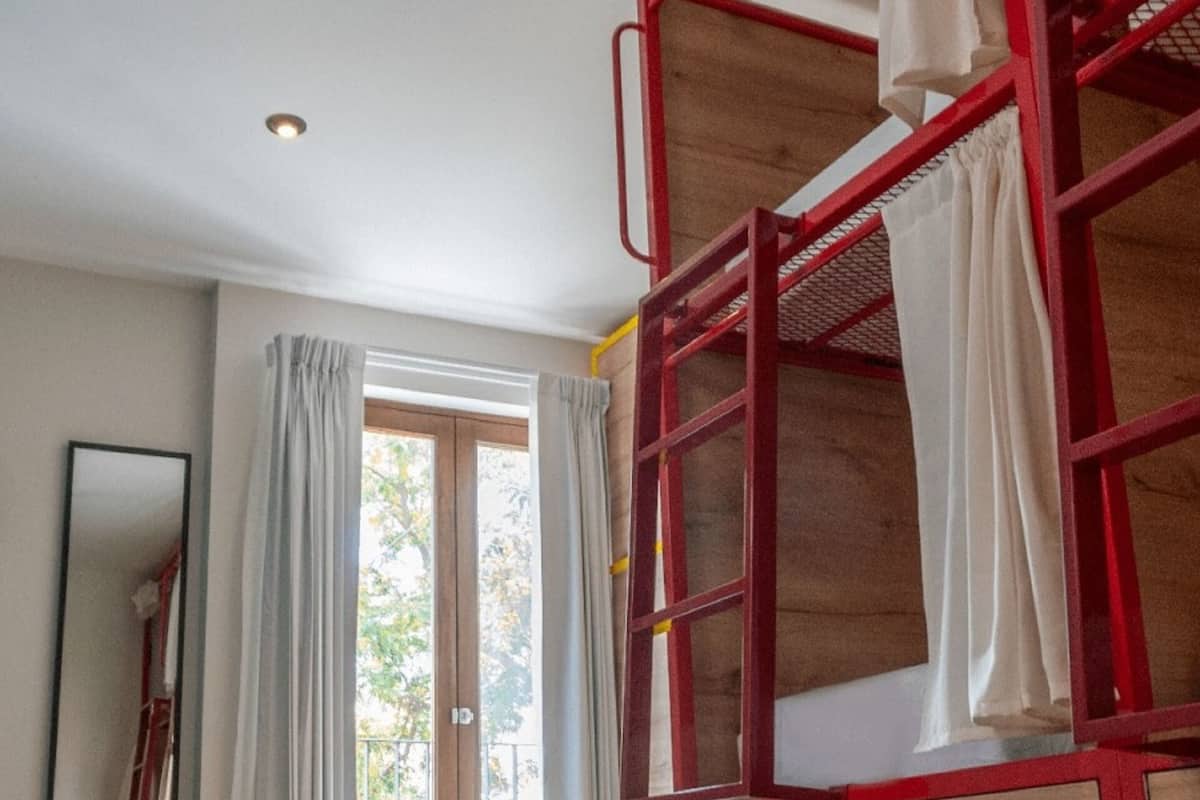 A room with bunk beds, a large window with curtains, a mirror, and a yellow wall.