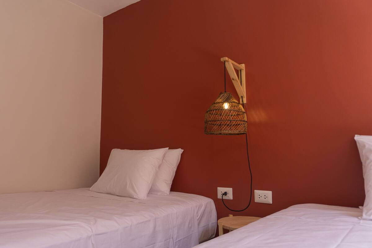 A room with two single beds, a red accent wall, and a hanging light fixture.