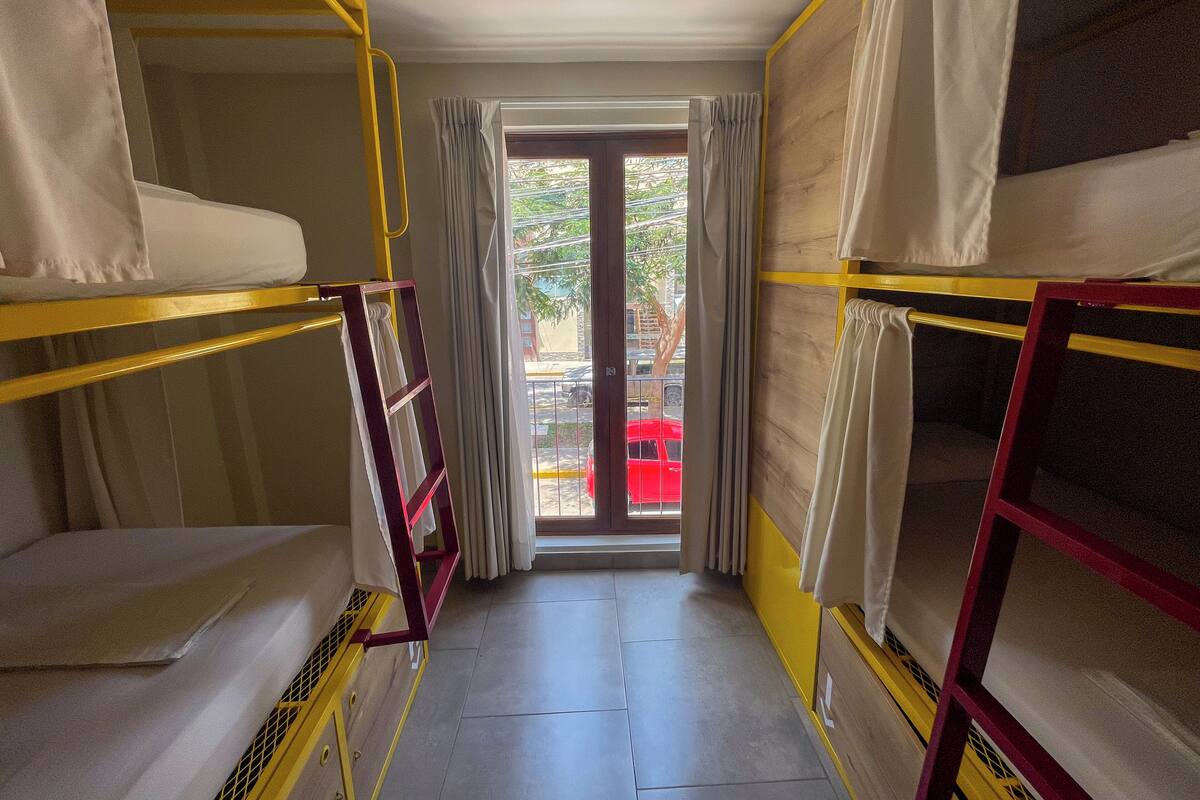 A corridor with bunk beds, a door leading outside, and a view of a red car through the window.