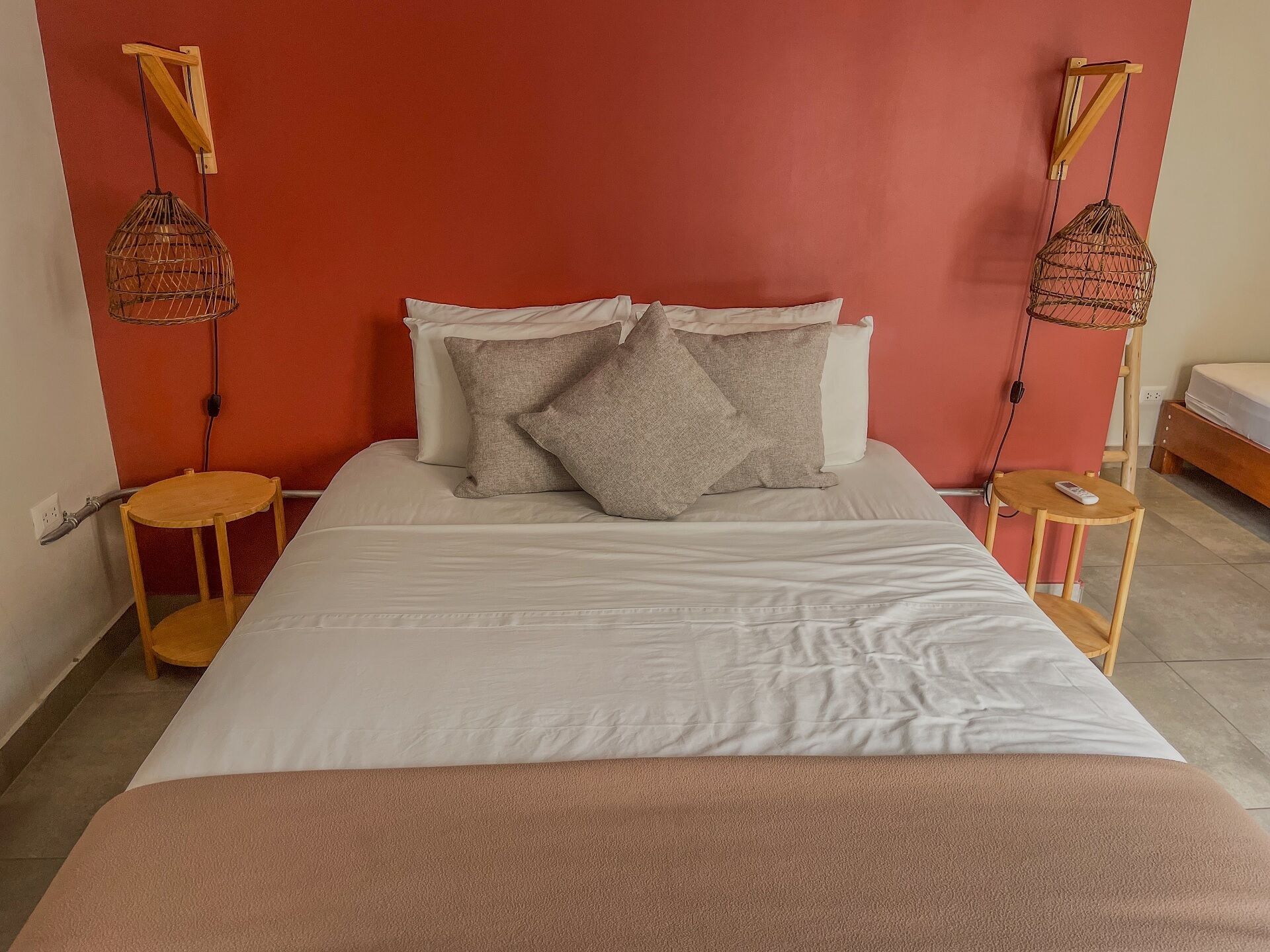 Una cama bien hecha con sábanas blancas y una manta rosa, flanqueada por dos mesitas de noche de madera con lámparas.