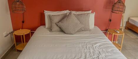 Una cama bien hecha con sábanas blancas y una manta rosa, flanqueada por dos mesitas de noche de madera con lámparas.