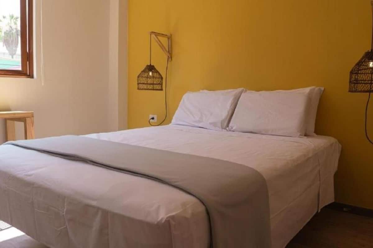 A bed in a room with yellow walls, a window, and two wall-mounted lamps.