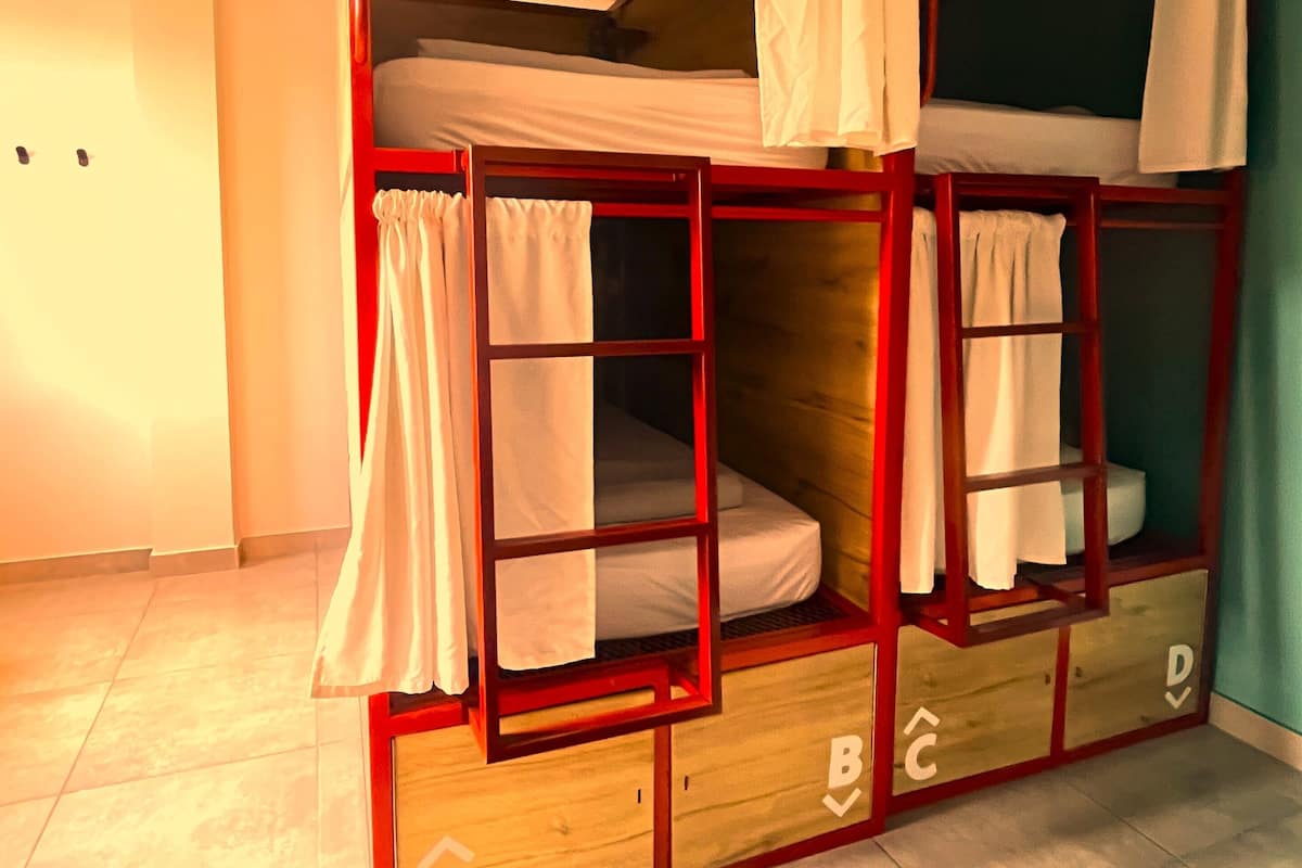 A bunk bed room with a red frame, white bedding, and a ceiling light.