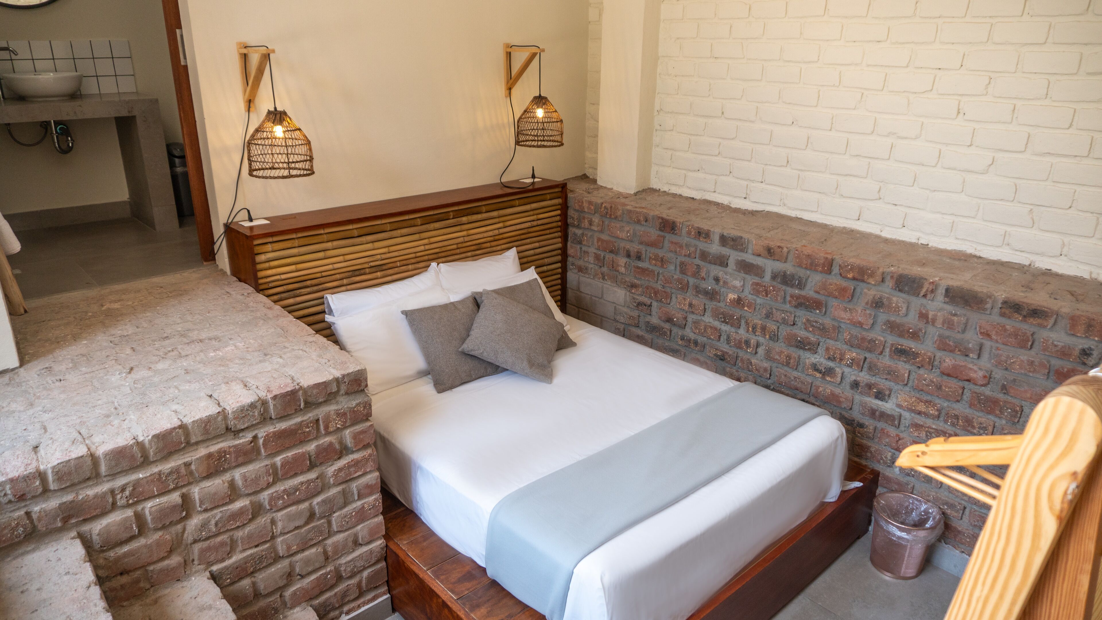 A bed with a wooden headboard, two bedside lamps, and a brick accent wall.