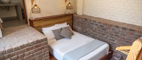 A bed with a wooden headboard, two bedside lamps, and a brick accent wall.