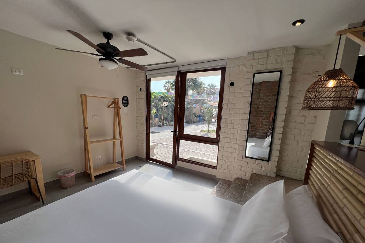 A bedroom with a bed, a ceiling fan, a wooden dresser, a mirror, and a view of the outside.