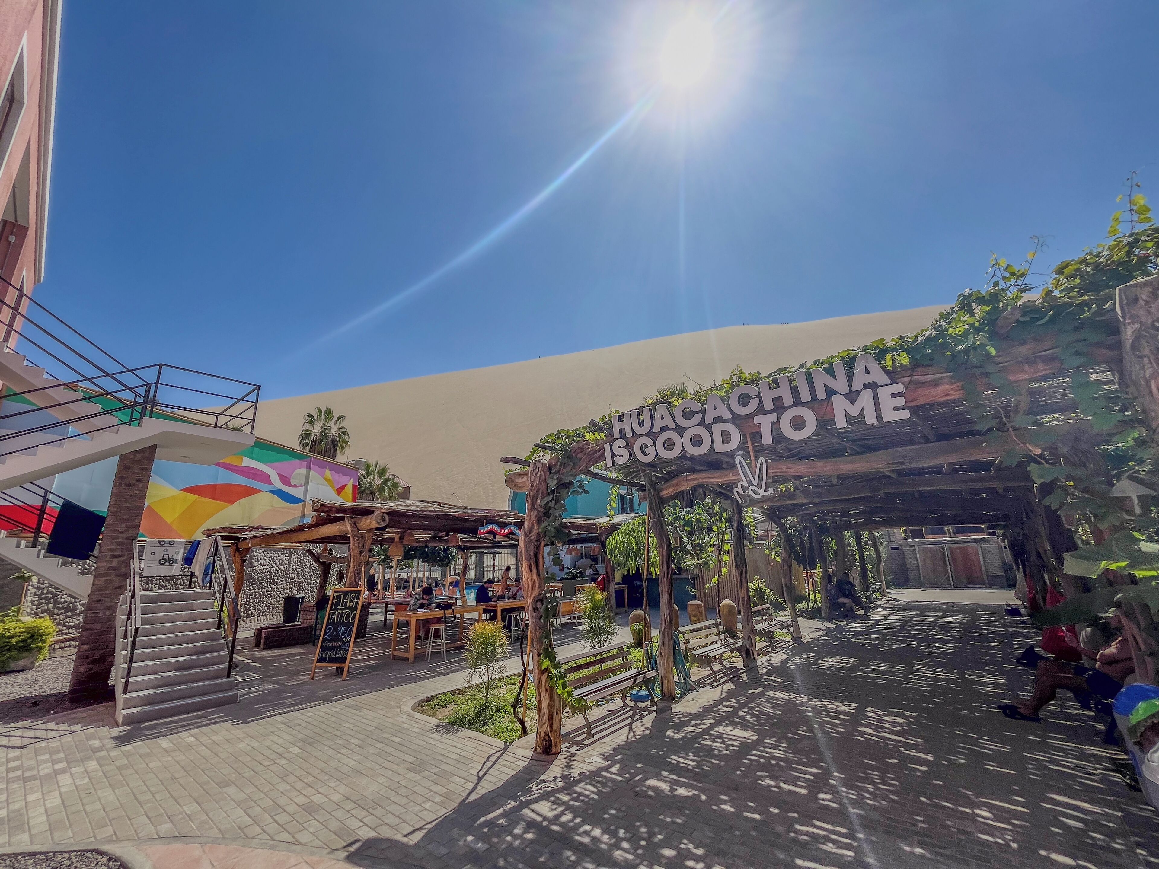 An outdoor area with a sign that reads "HUACACHINA IS GOOD TO ME" and a mural in the background.