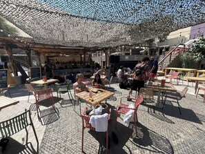 An outdoor café with tables and chairs, a covered seating area, and a staircase in the background. - Viajero Huacachina Hostel (Ica)
