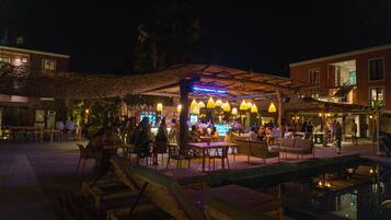 An outdoor dining area with tables and chairs, a pool, and a covered seating area with hanging lights.