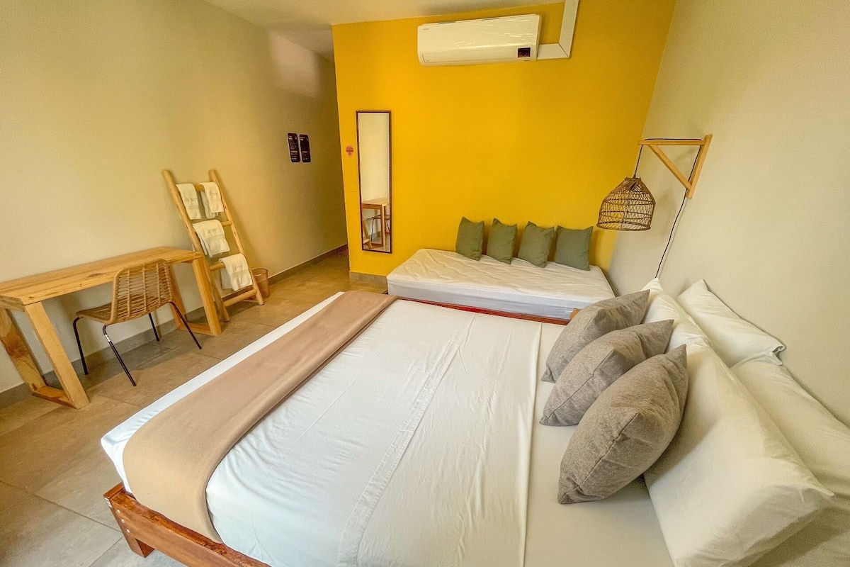 A bedroom with a bed, a desk, a chair, and a hanging light fixture.
