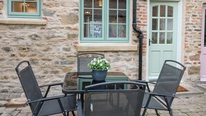 A stone building with a green door and windows, a small table with chairs, and a potted plant. - Bay Tree Cottage (Richmond)