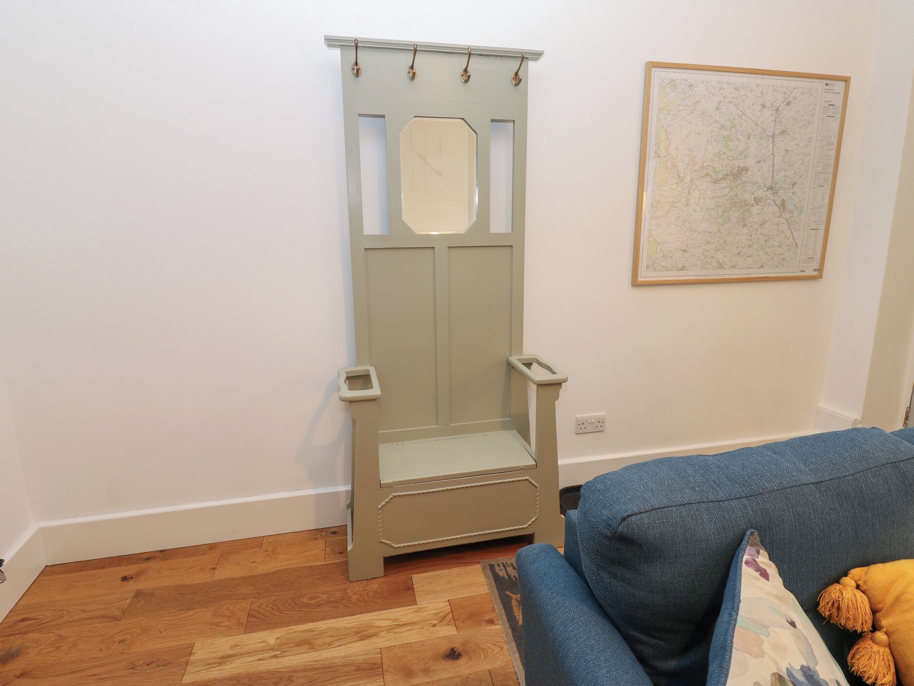 A room with a wooden floor, a blue sofa, a map on the wall, and a door with a handle.
