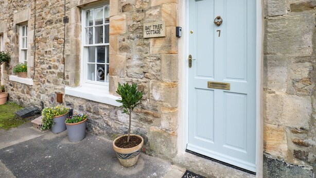 A stone building with a light blue door, a sign reading "Bay Tree Cottage", and several potted plants outside. - Bay Tree Cottage (Richmond)