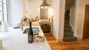 A modern kitchen with a stainless steel range hood, a built-in oven, and a large window providing natural light. - Bay Tree Cottage (Richmond)