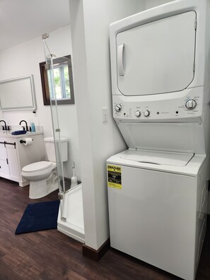 Et vaskerum med en frontindlæsningsvaskemaskine og tørretumbler, et toilet og en håndvask med et spejl over.