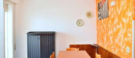 A dining area with a wooden table and chairs, a dark cabinet, and a wall with a textured orange finish and two decorative plates.