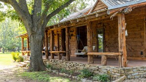 A rustic log cabin with a porch, stone foundation, and outdoor seating area.