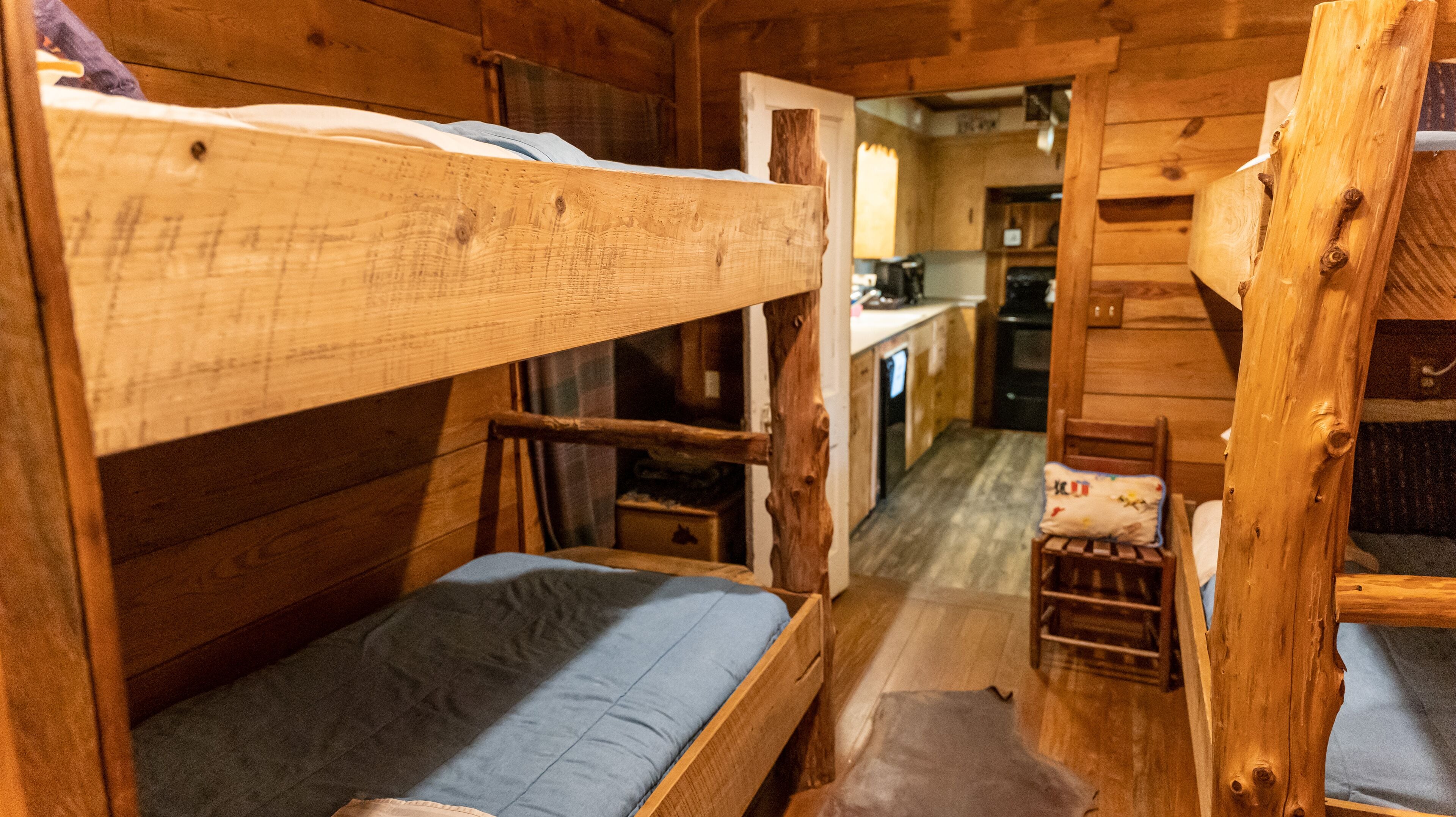 A cabin interior with wooden walls and floors, a bunk bed, a small kitchenette, and a dining area.