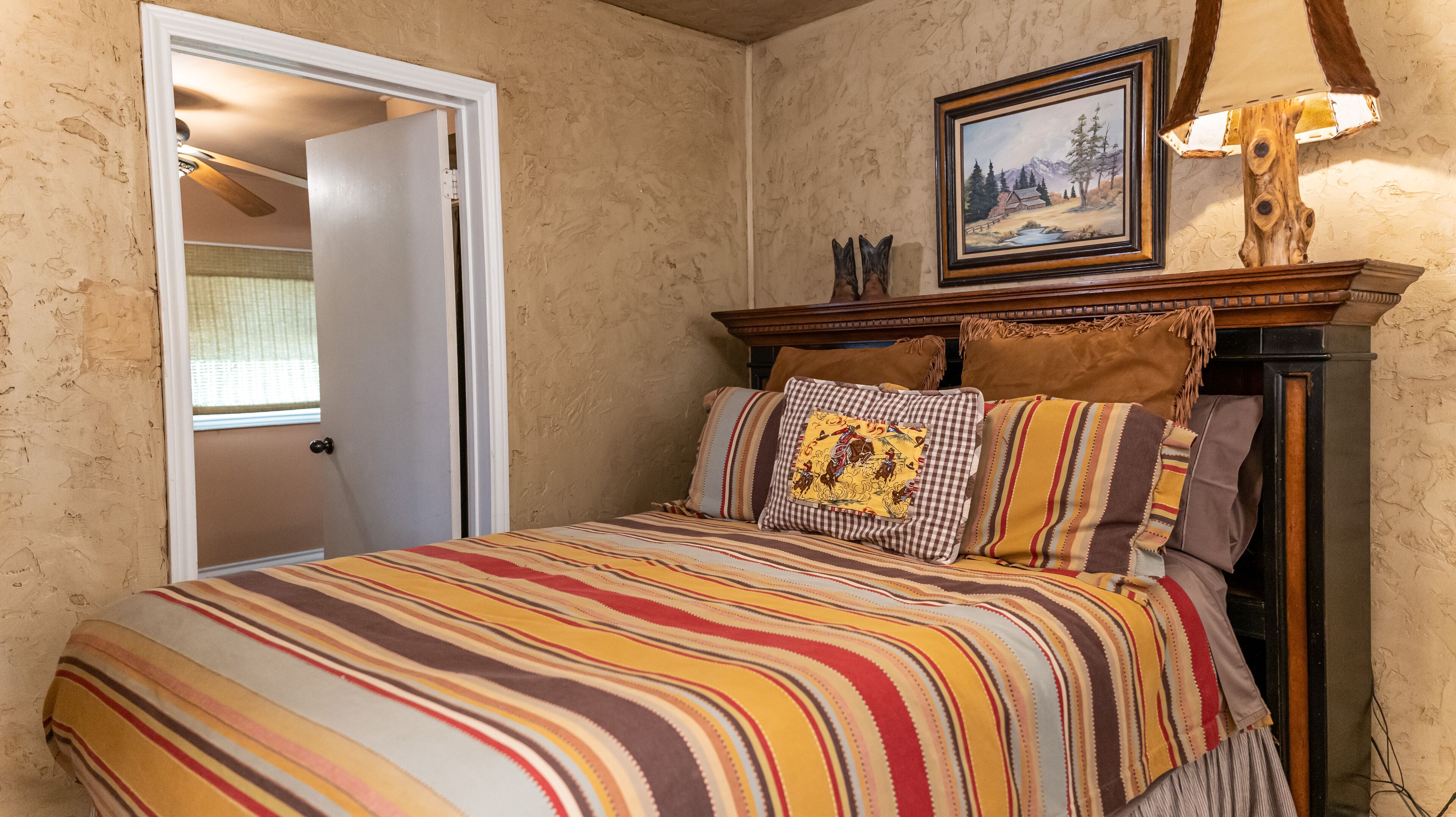 A bedroom with a striped bedspread, a wooden headboard, and a painting above the bed.