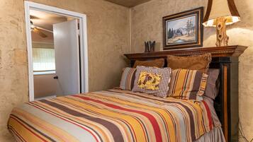A bedroom with a striped bedspread, a wooden headboard, and a painting above the bed.