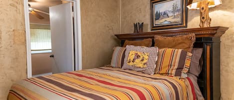 A bedroom with a striped bedspread, a wooden headboard, and a painting above the bed.