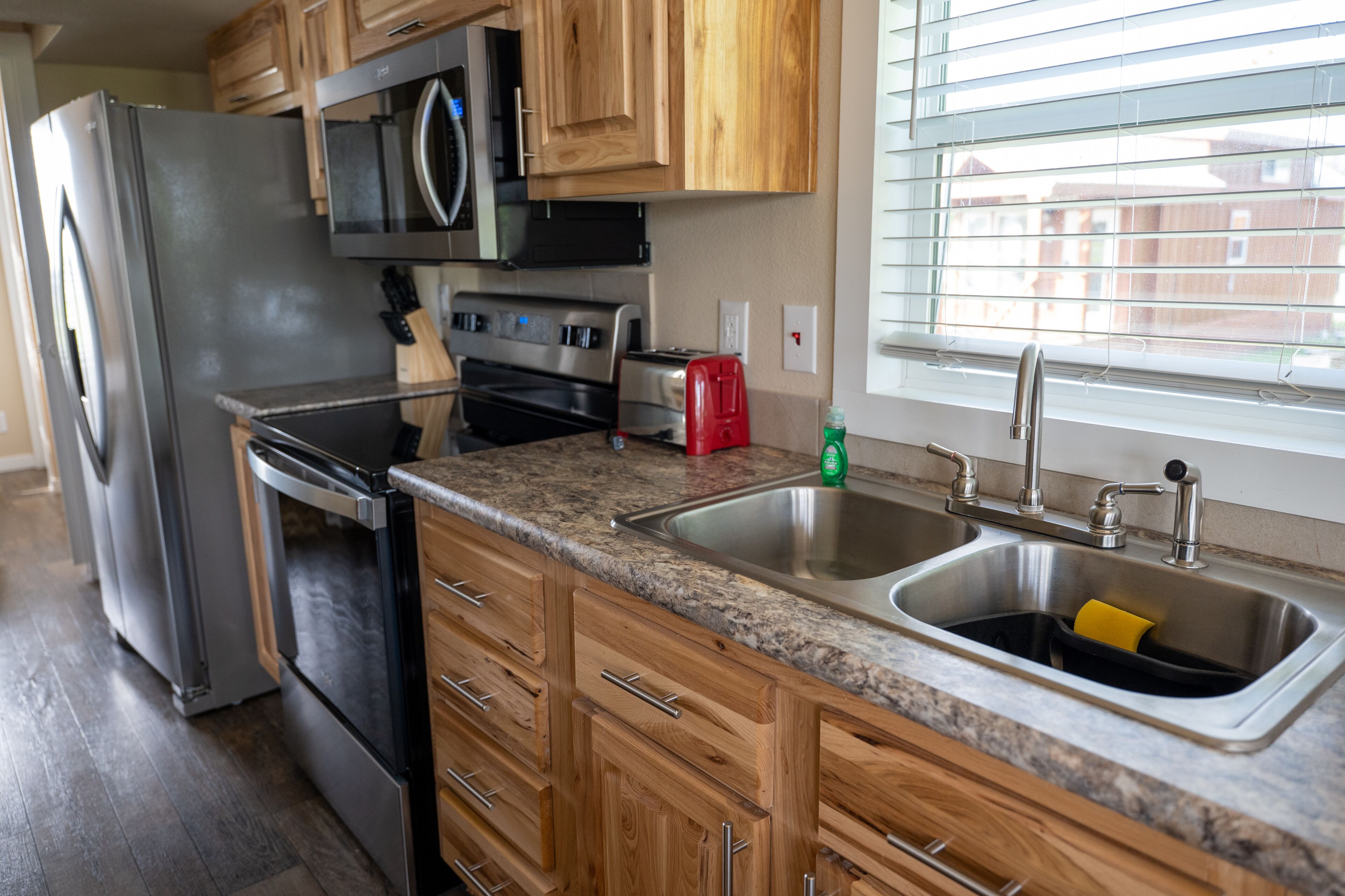 A kitchen with wooden cabinets, a stainless steel refrigerator, a microwave, a stove, and a sink.