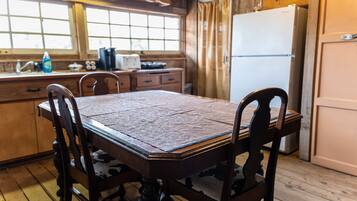 A wooden dining table with chairs, a window with curtains, a refrigerator, and a kitchen counter with appliances.