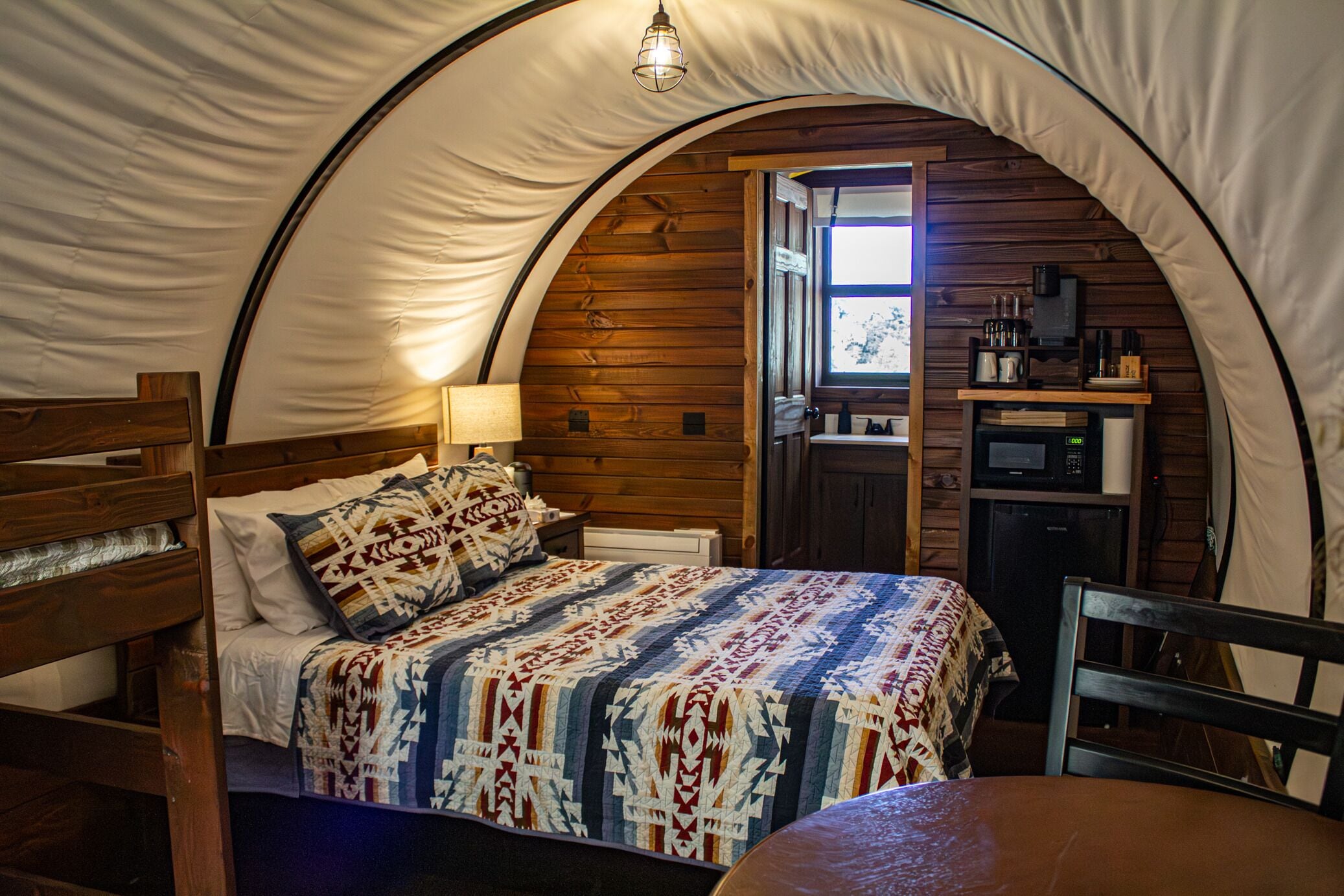 A cozy tent with a bed, a table, a chair, and a kitchenette area.