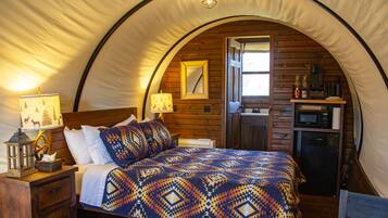 A tented accommodation with a bed, bedside lamps, a small kitchenette, and a wooden interior.