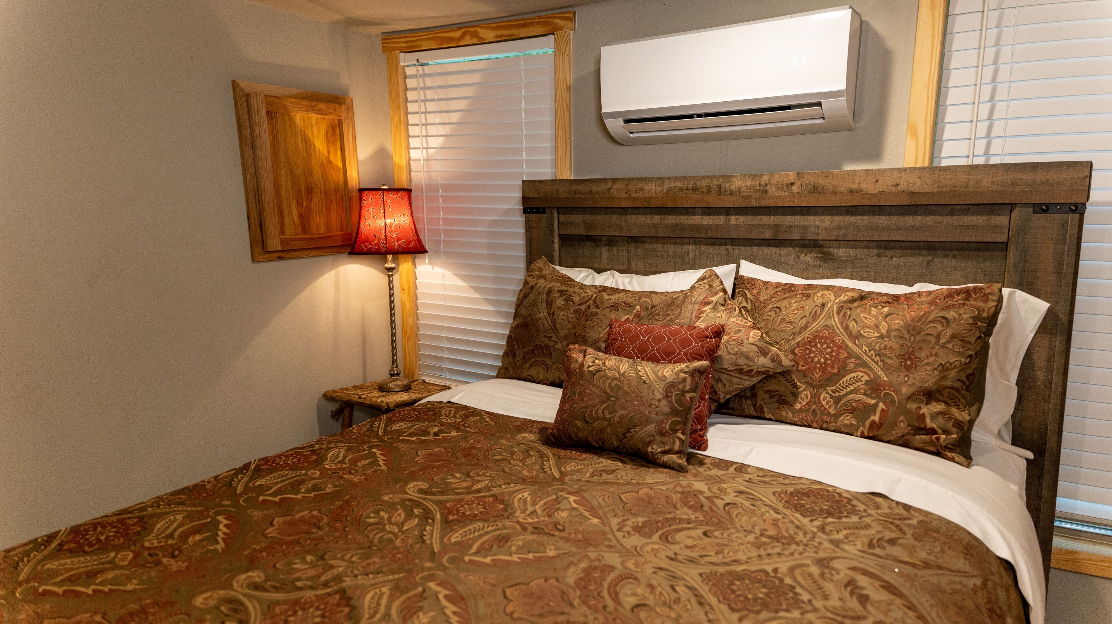 Un lit avec une literie à motifs, une tête de lit en bois, une lampe de chevet et un appareil de climatisation fixé au mur.