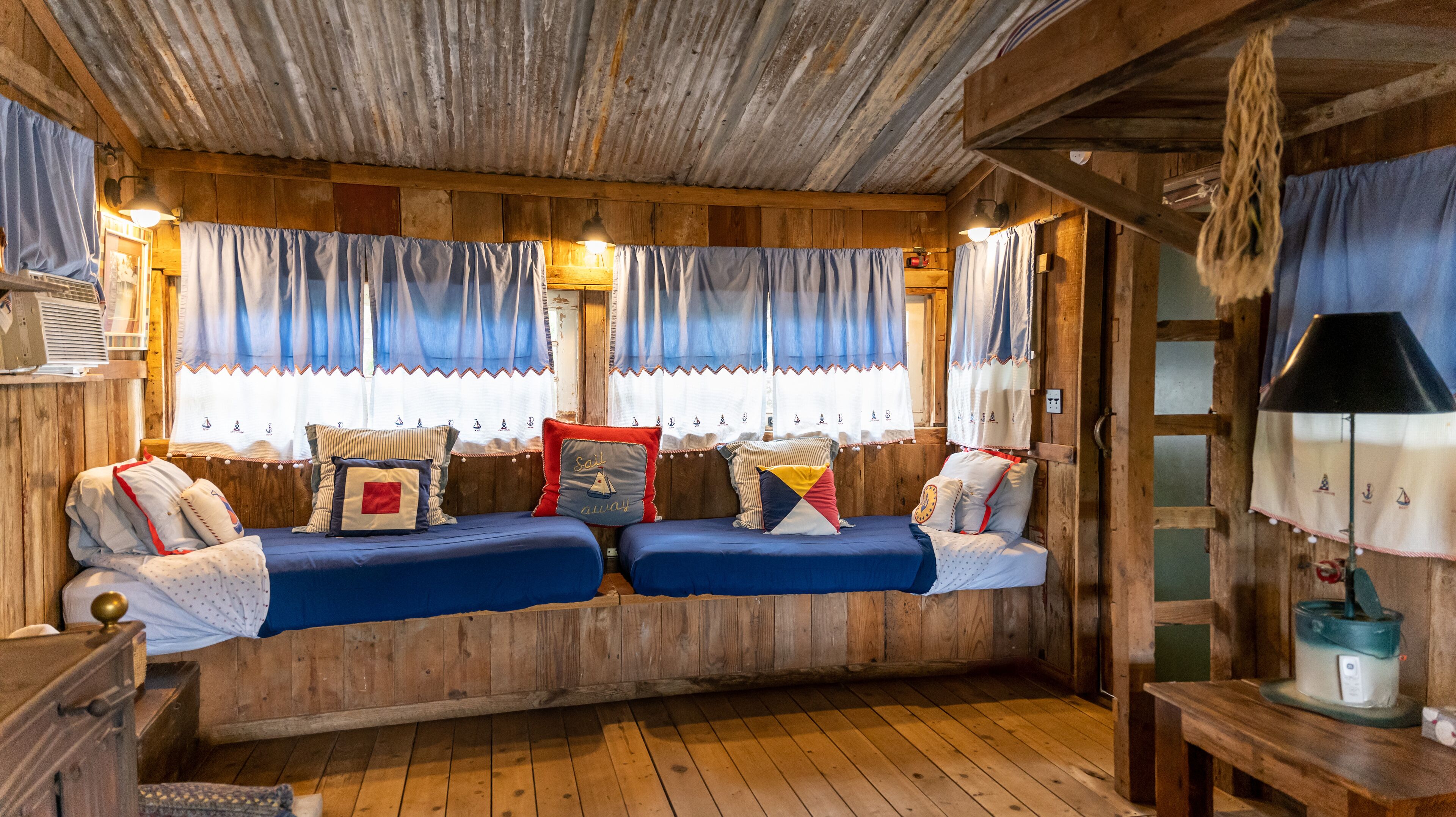 A cabin with a wooden interior, two beds with blue bedding, and a rustic aesthetic.