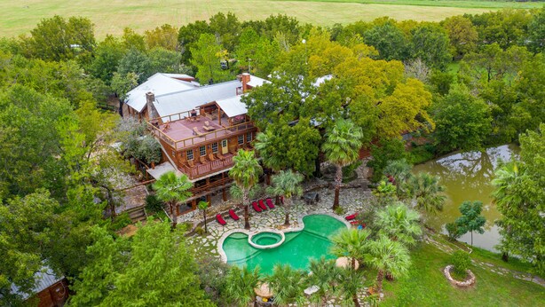 A large house with a pool, surrounded by trees and a pond.