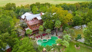 Una casa grande con piscina, rodeada de árboles y un estanque.
