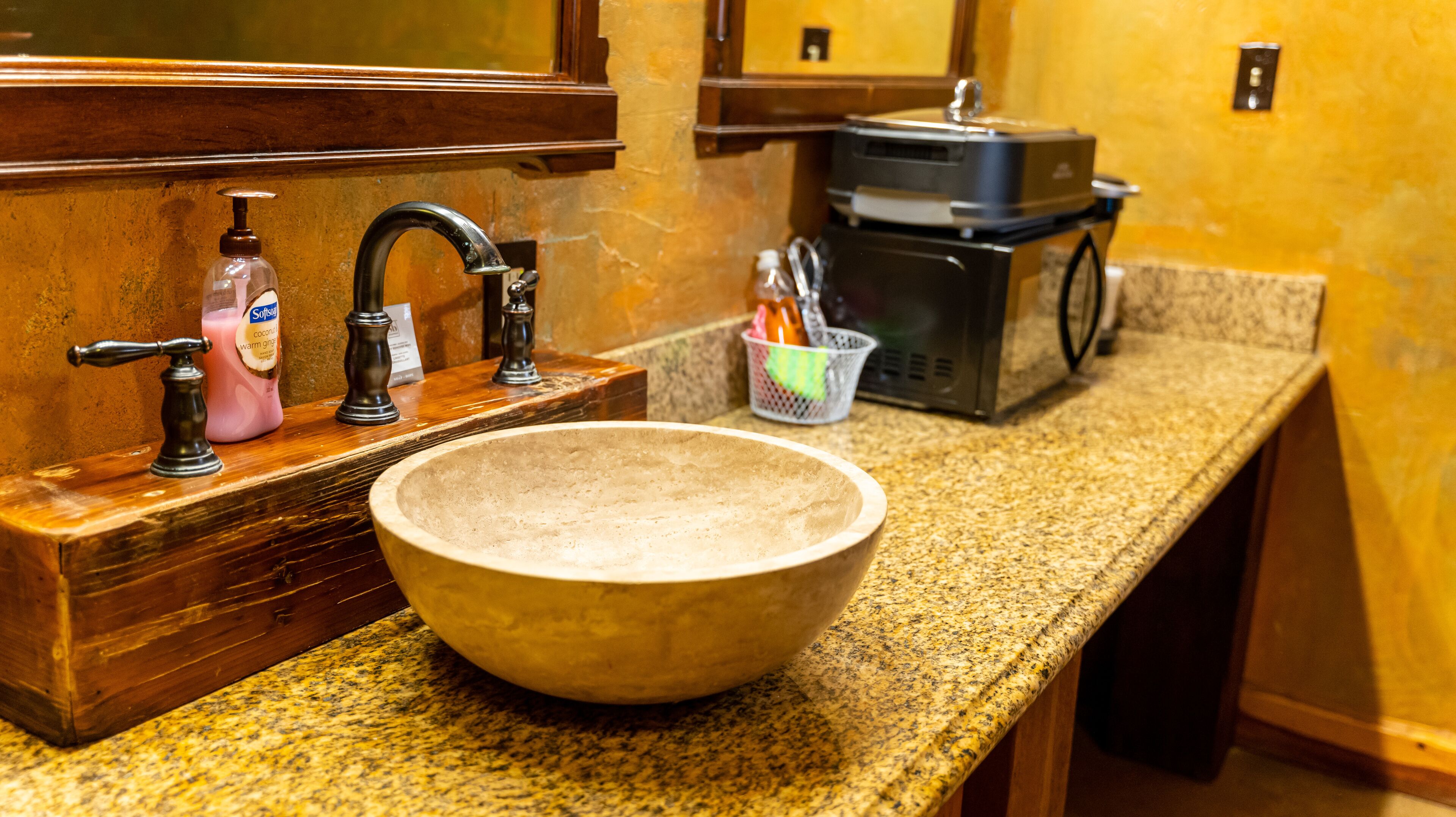 A kitchen with a granite countertop, a wooden sink, a soap dispenser, and a coffee maker.