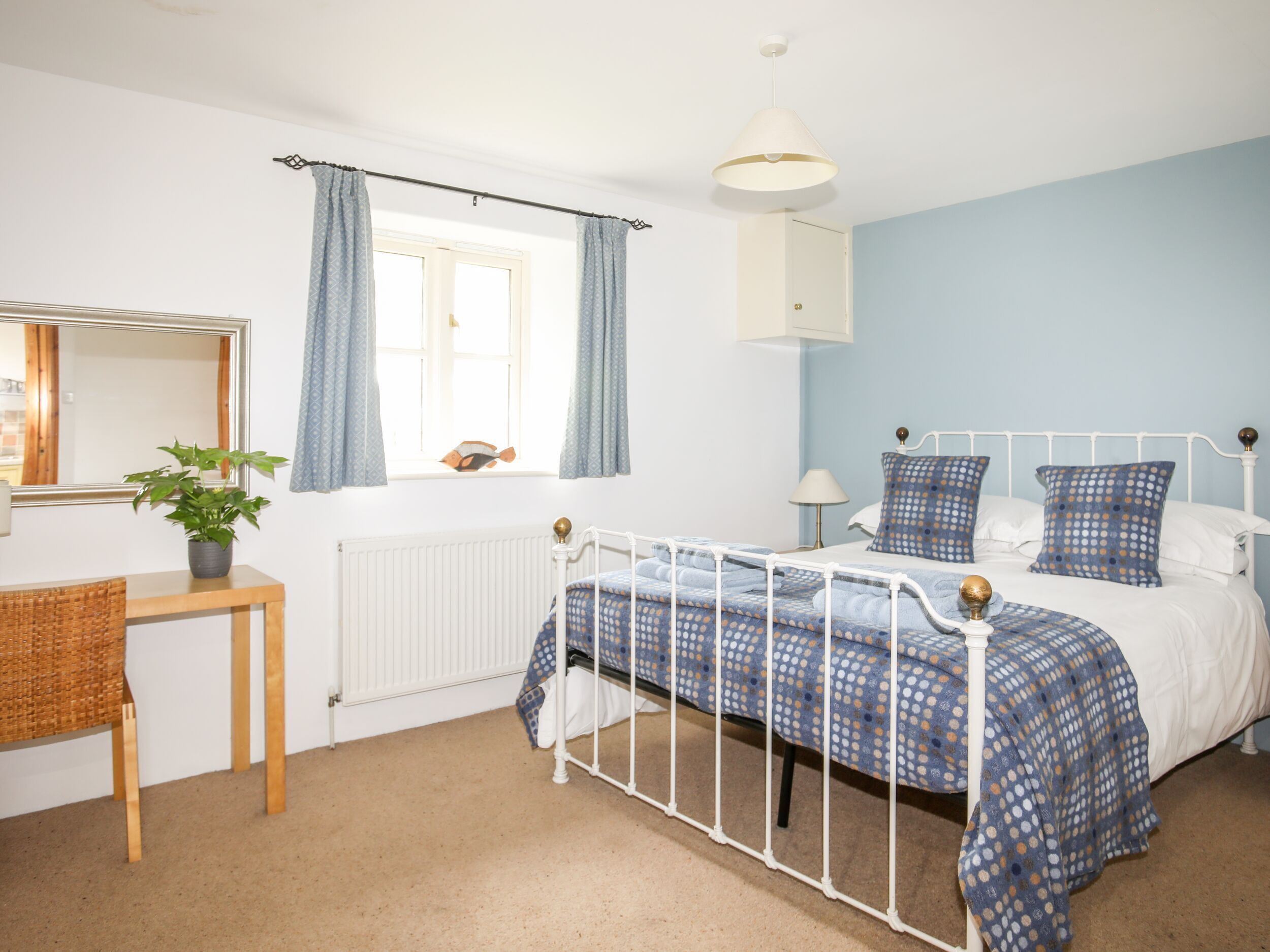 A bedroom with a bed, a bedside table, a mirror, a window with curtains, and a radiator.