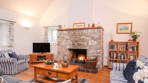 A cozy living room with a stone fireplace, striped sofas, a wooden coffee table, and a bookshelf. - Rhyd Y Bont Bach (Holyhead)