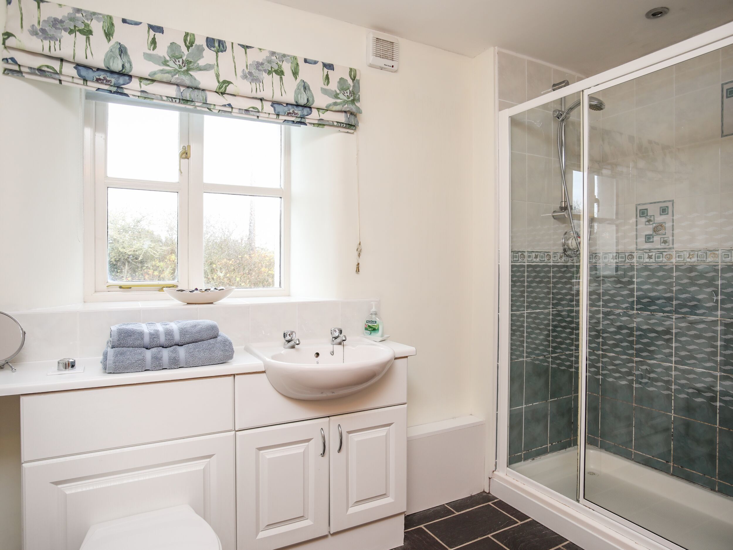 Ein Badezimmer mit Fenster, Waschbecken, Toilette und Duschbereich.