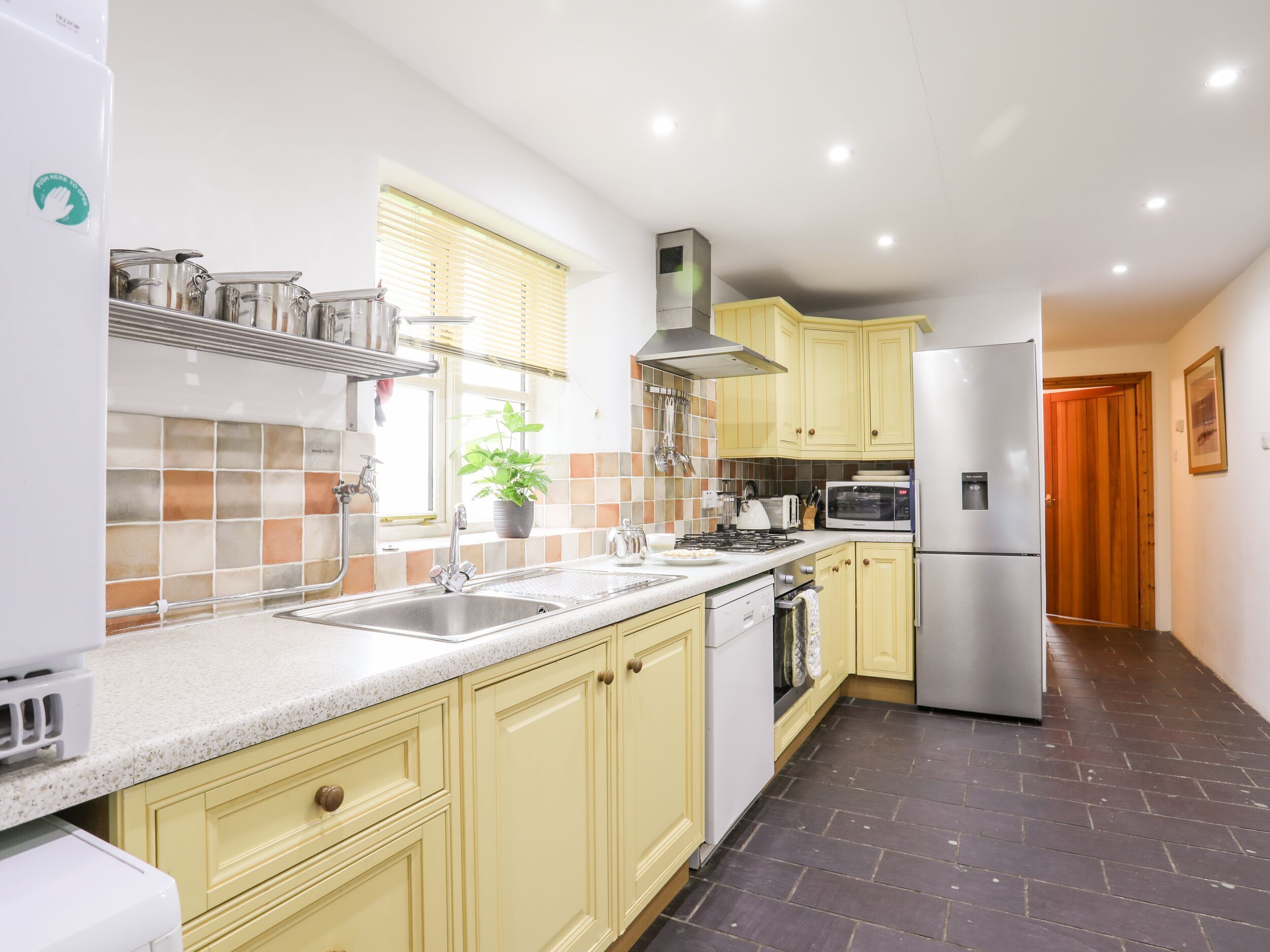 A kitchen with yellow cabinets, a stainless steel sink, a microwave, and a refrigerator.