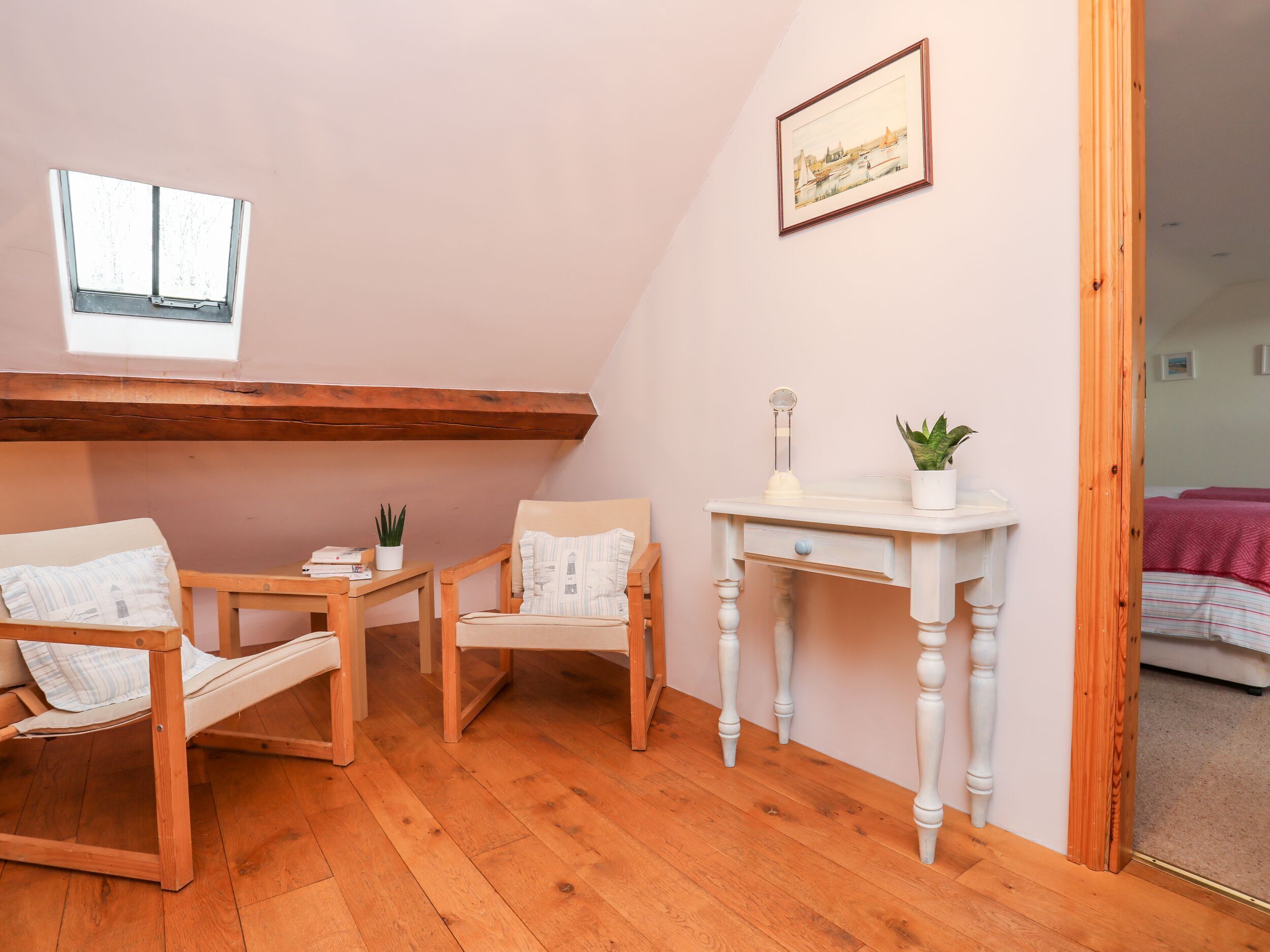 A cozy room with a wooden floor, two chairs, a small table, a potted plant, and a framed picture on the wall.