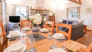 A dining area with a wooden table set for four, surrounded by wooden chairs. A vase with white flowers is on the table. - Rhyd Y Bont Bach (Holyhead)