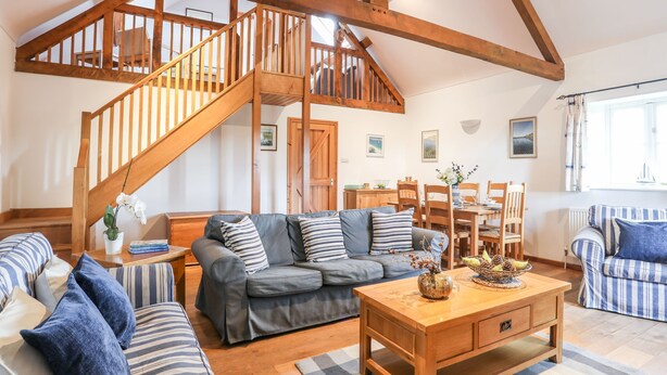 A spacious living room with a high wooden ceiling, a staircase, a dining area, and a view of the outdoors. - Rhyd Y Bont Bach (Holyhead)
