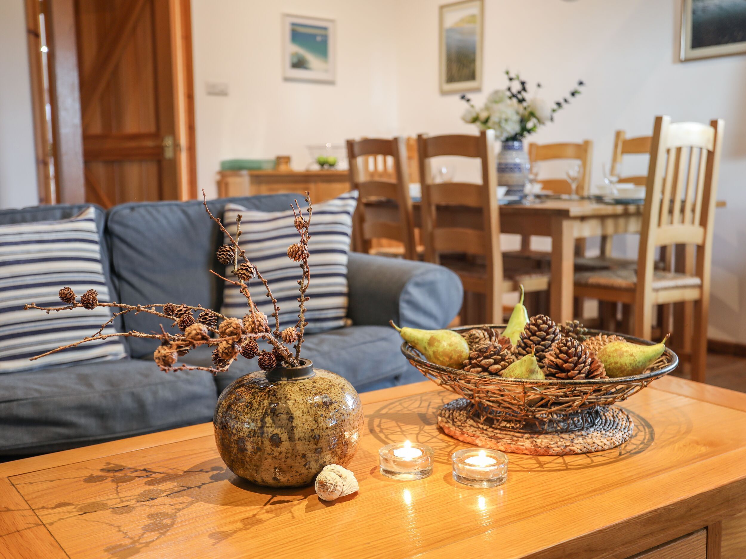 Een woonkamer met een bank, een salontafel met een vaas en kaarsen, en een eethoek op de achtergrond.