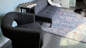 Un salon avec un canapé gris, un fauteuil noir, une télévision et un meuble.