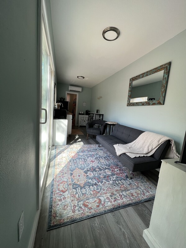 A modern living room with a grey sofa, a patterned rug, and a large mirror on the wall.