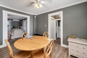 A dining area with a round wooden table, four chairs, a ceiling fan, and a white dresser with drawers.