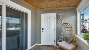 A room with a sliding glass door, a white door, a wicker chair, and a window with a view of buildings. - The Whale Spout - King bed and close to the Beach! (Hampton)