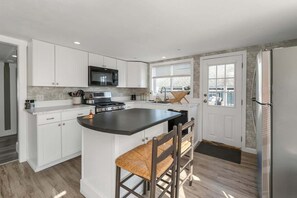 A modern kitchen with white cabinets, a central island, a microwave, and a refrigerator.