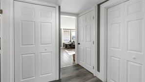 A hallway with white doors leading to a room with a wooden floor and a view of an outdoor area. - The Salty Oyster - Amazing Deck and Short Walk to beach! (Hampton)